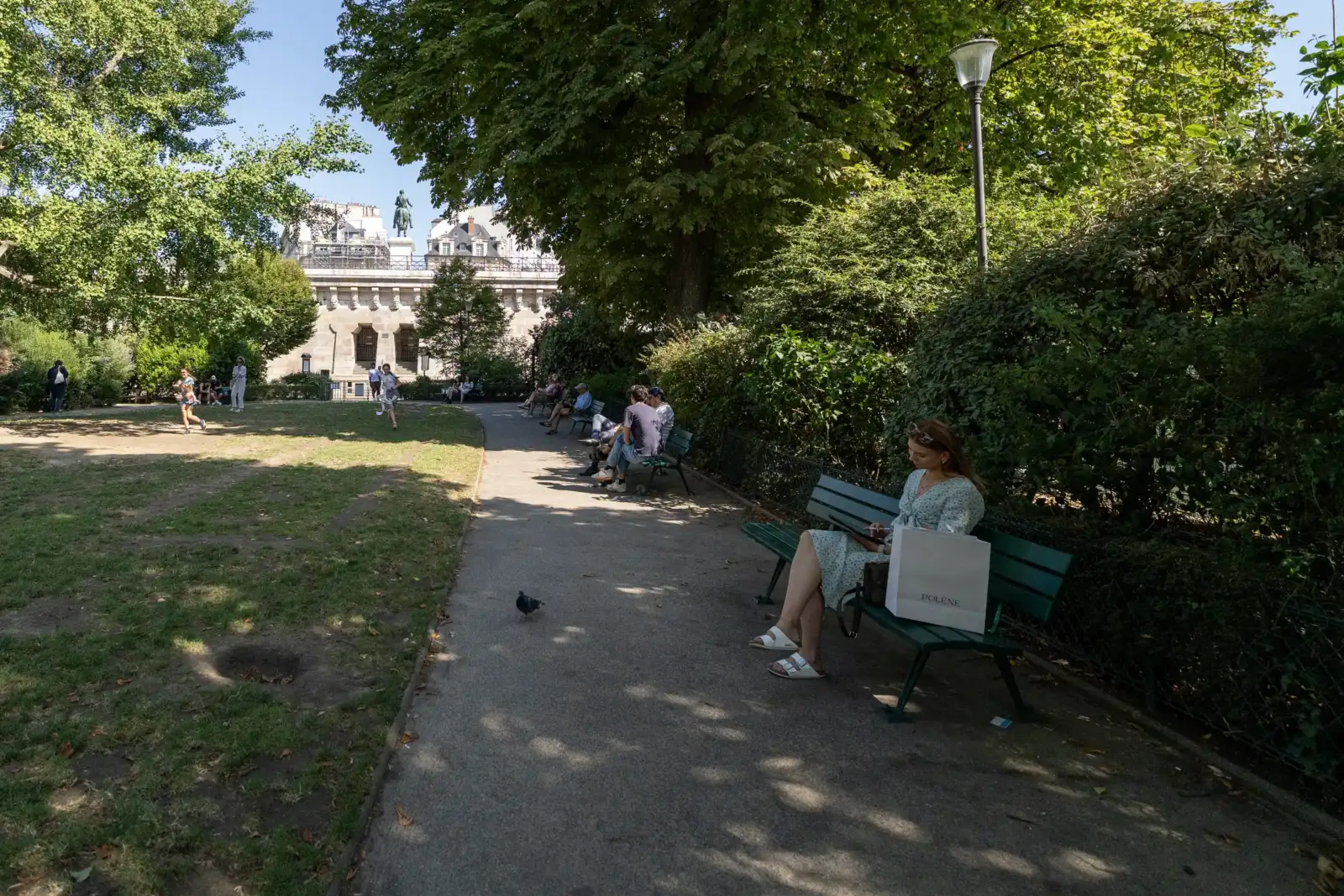 Une femme assise sur un banc vert dans un parc parisien ombragé.