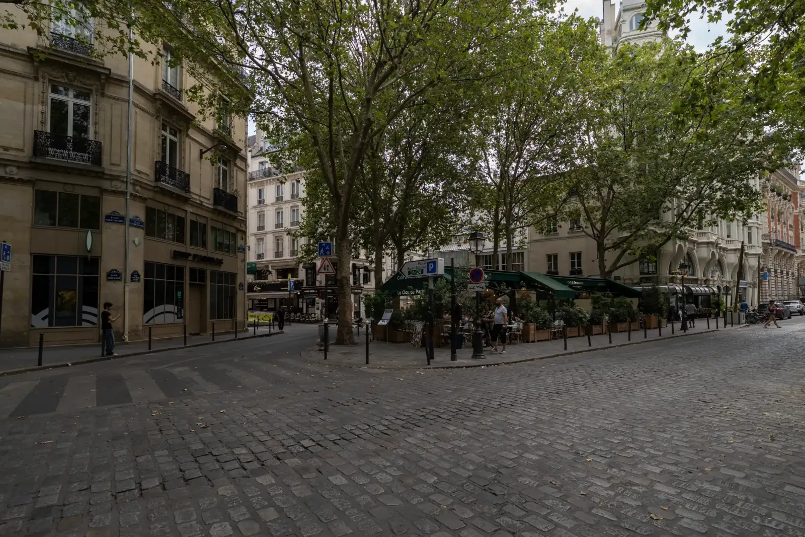 Vue de rue pavée à Paris montrant des immeubles haussmanniens et des arbres verdoyants.