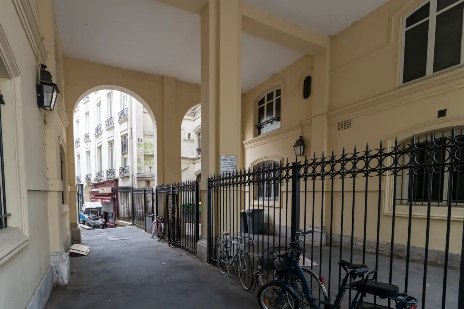 Vue depuis un porche vouté beige vers une rue parisienne animée.