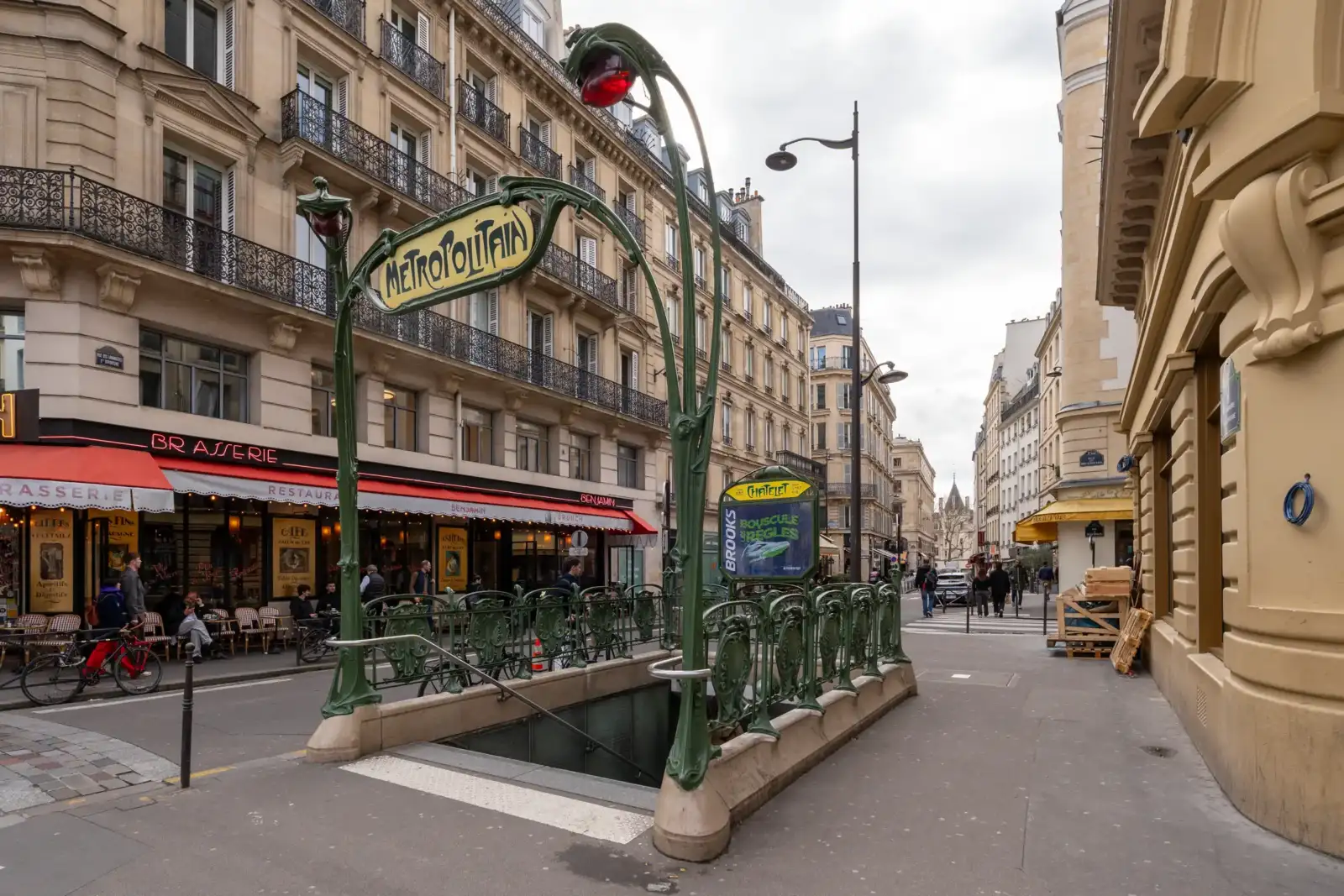 Entrée de métro Art nouveau typique située sur un trottoir dans une rue parisienne.