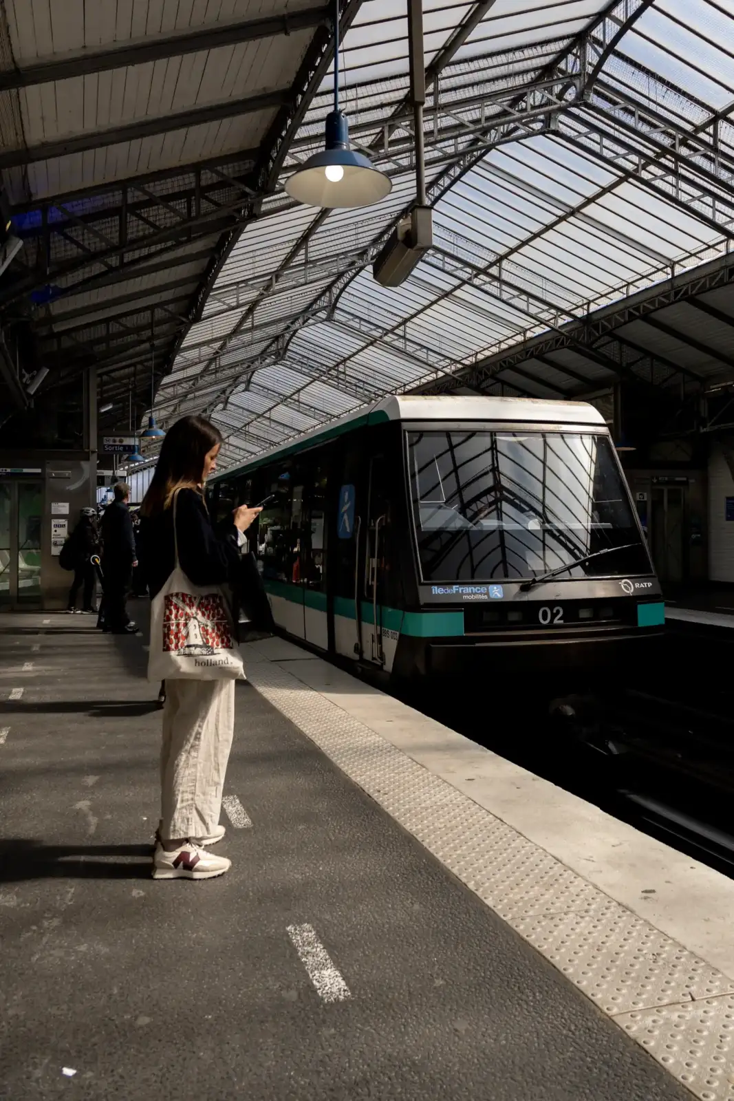 Une femme attend un métro parisien sous une verrière lumineuse dans une station moderne.