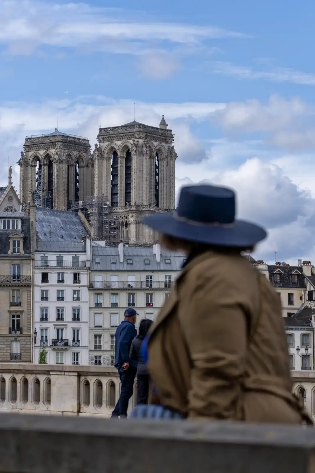 Une personne au premier plan observe la cathédrale Notre-Dame sous un ciel nuageux parisien.