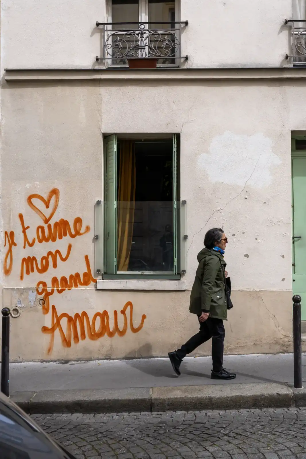 Une femme marche devant une façade parisienne ornée d'un graffiti romantique en orange.