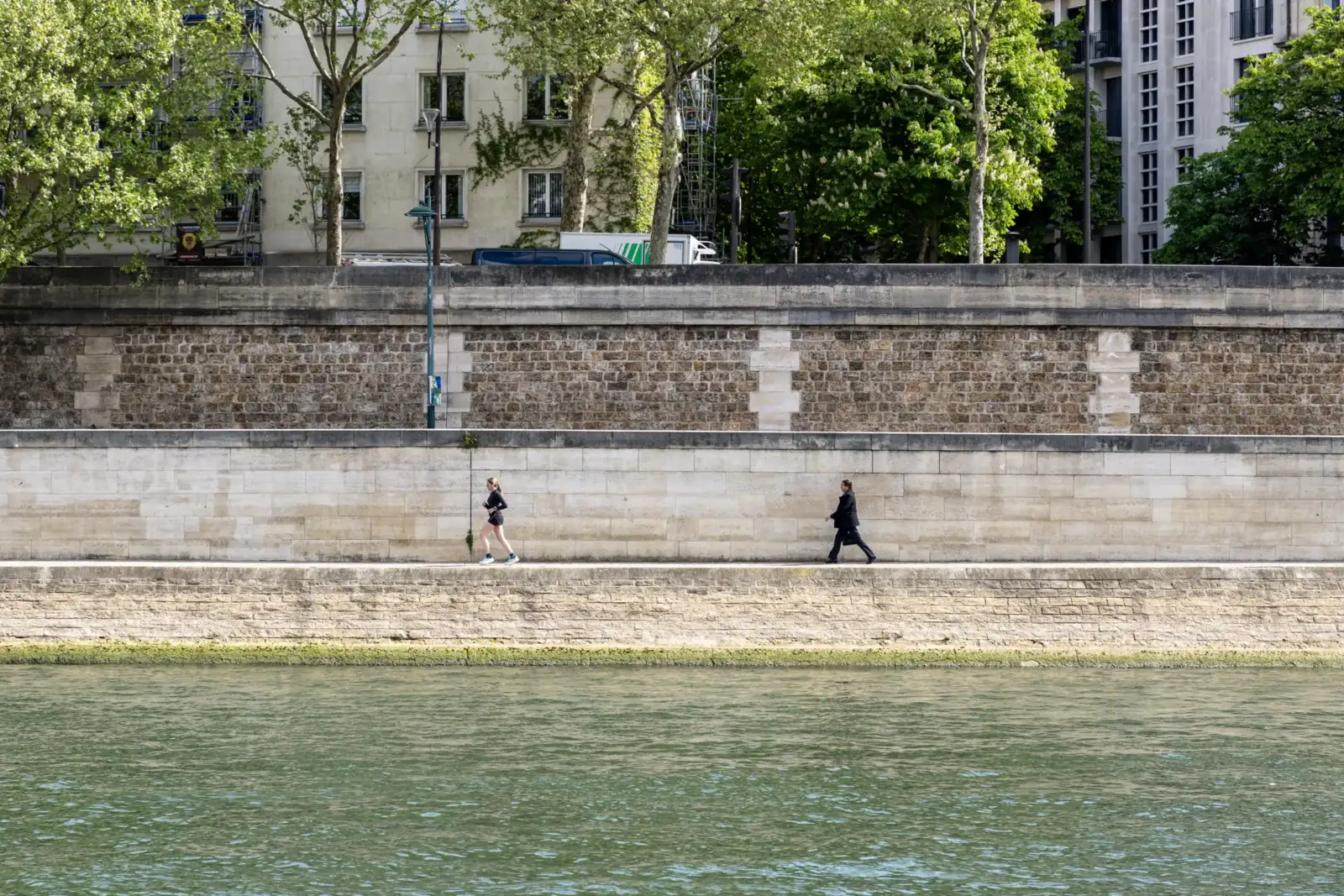Une femme court et un homme marche le long des quais de Seine parisiens.