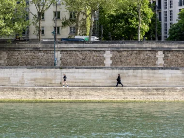 Une femme court et un homme marche le long des quais de Seine parisiens.