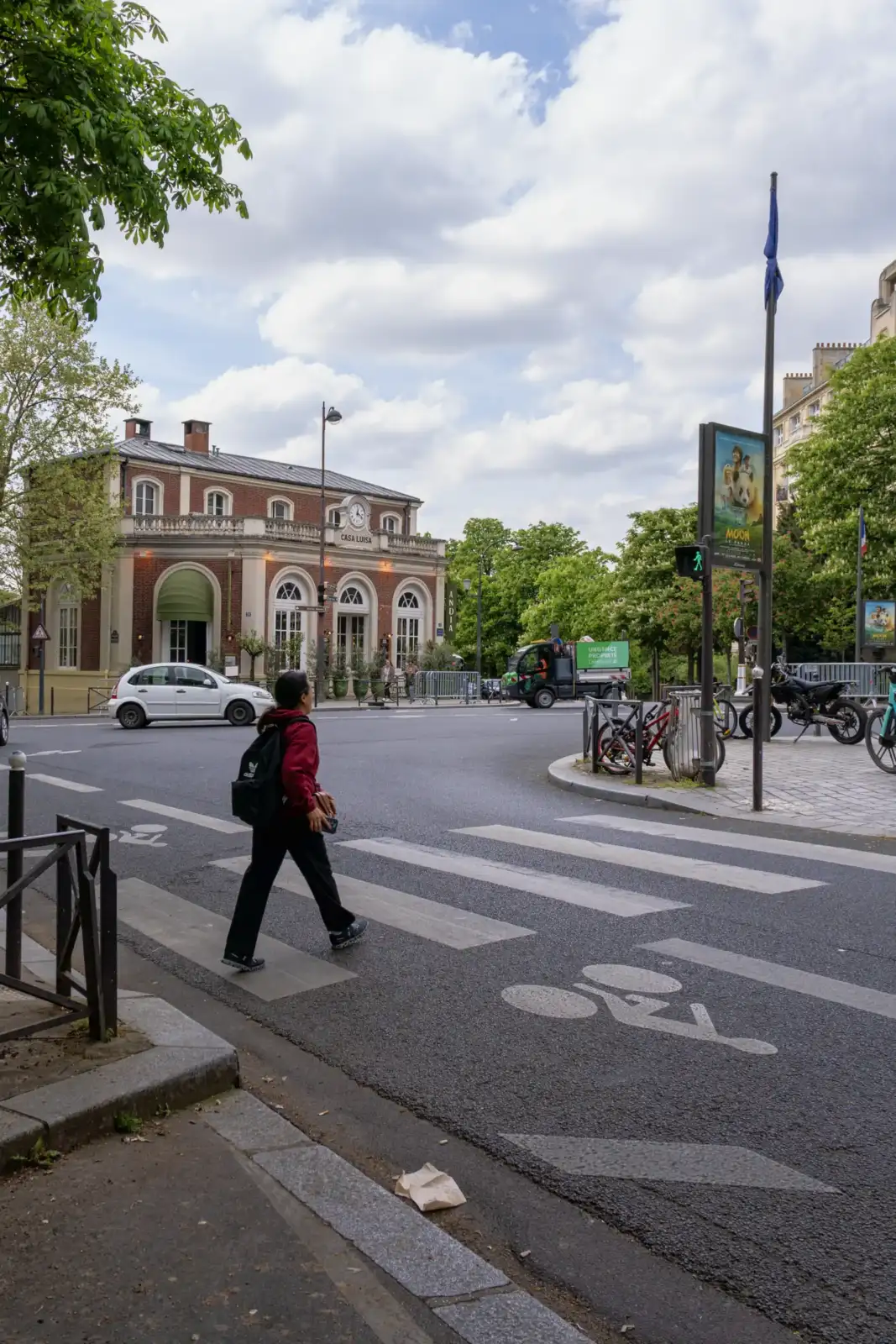 Une personne traverse une rue parisienne devant un bâtiment historique sous un ciel nuageux.