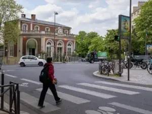 Une personne traverse une rue parisienne devant un bâtiment historique sous un ciel nuageux.