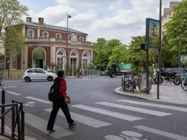 Une personne traverse une rue parisienne devant un bĂątiment historique sous un ciel nuageux.