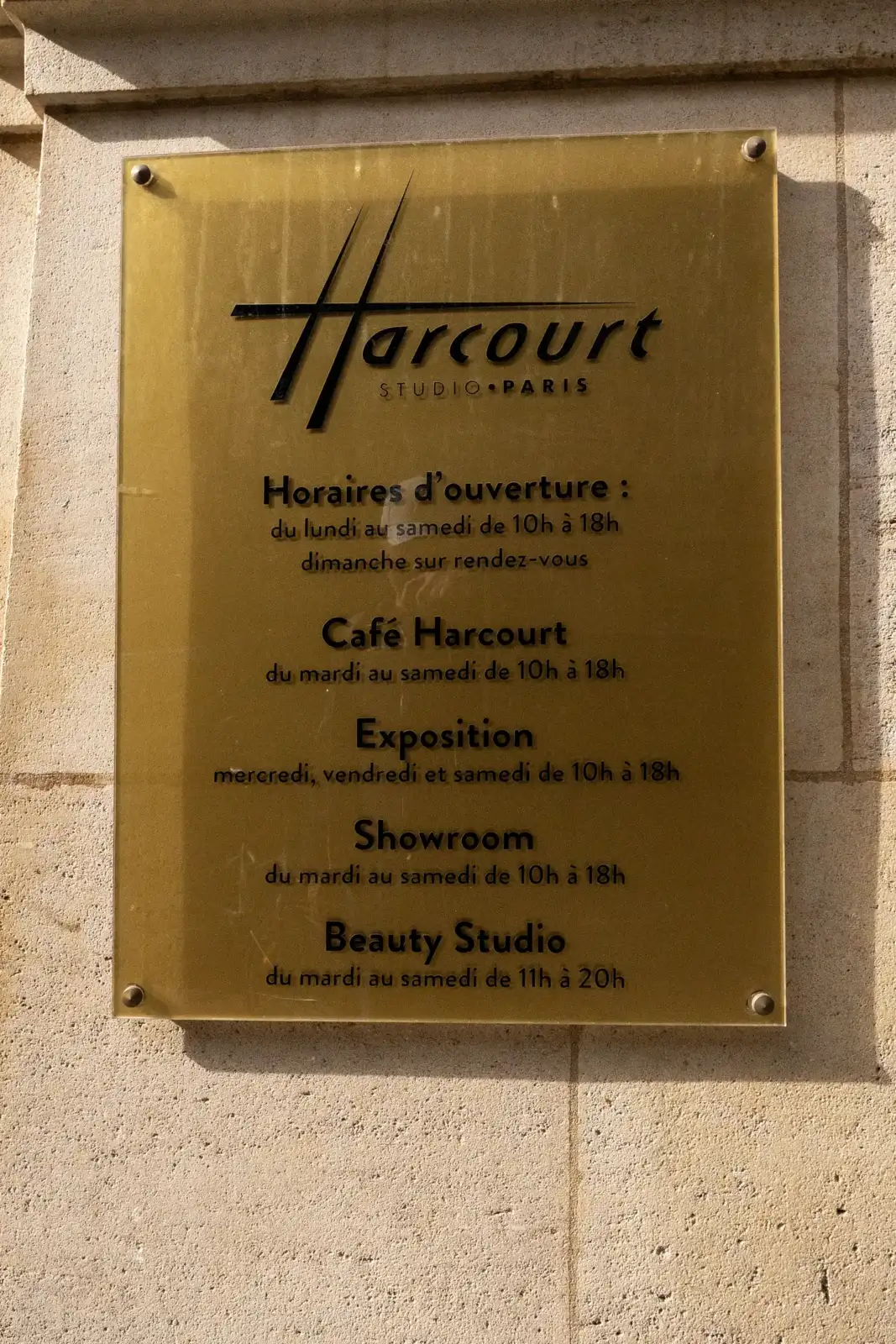 Une plaque dorée indique les horaires du célèbre Studio Harcourt Paris sur un mur.