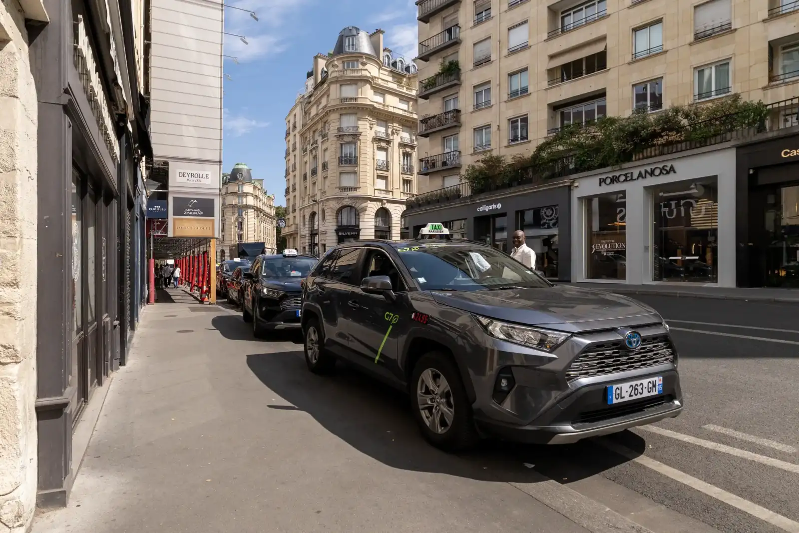 Un taxi gris est garé dans une rue parisienne bordée d'immeubles haussmanniens.