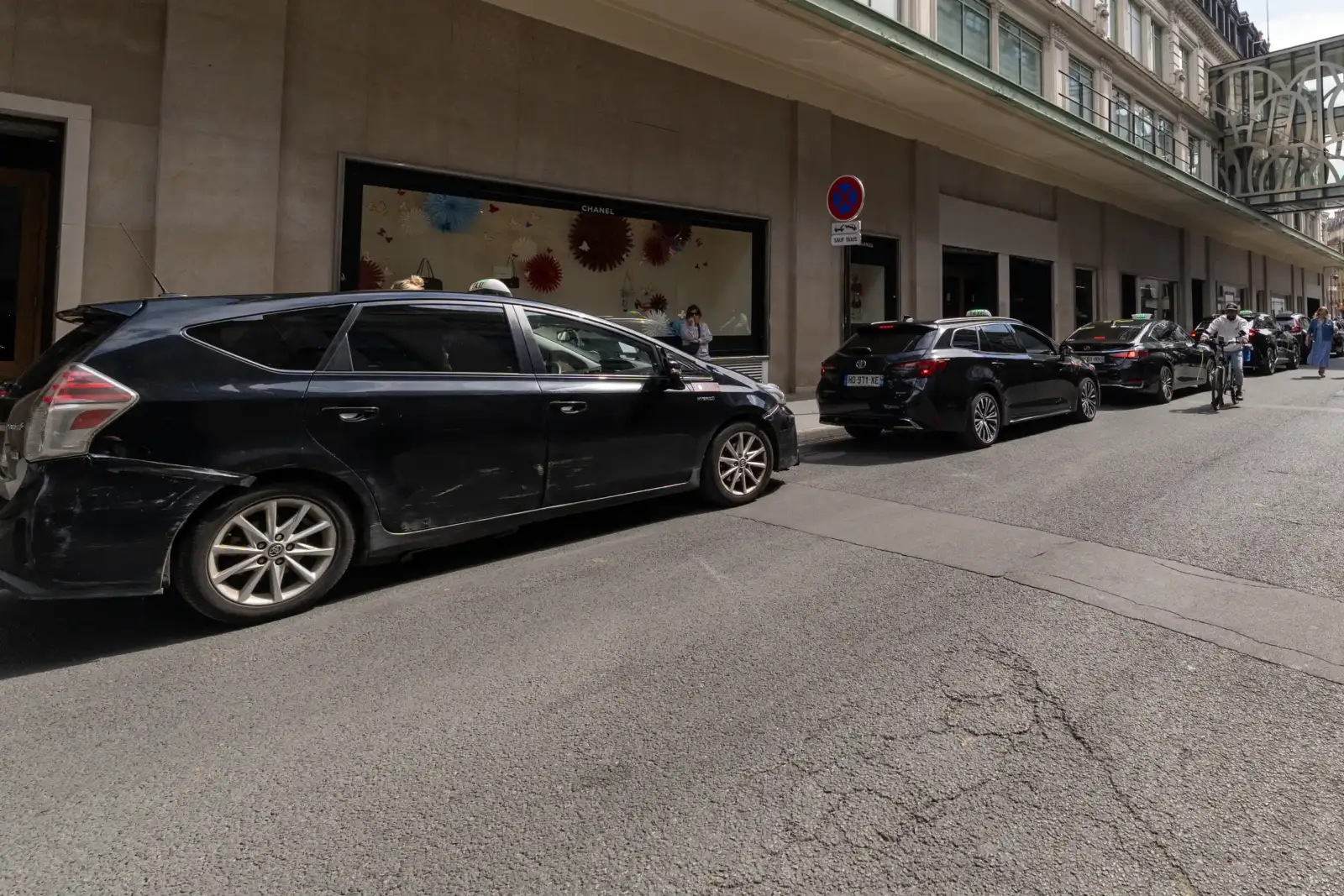 Des taxis noirs stationnent le long d une rue bordée par un grand immeuble parisien.