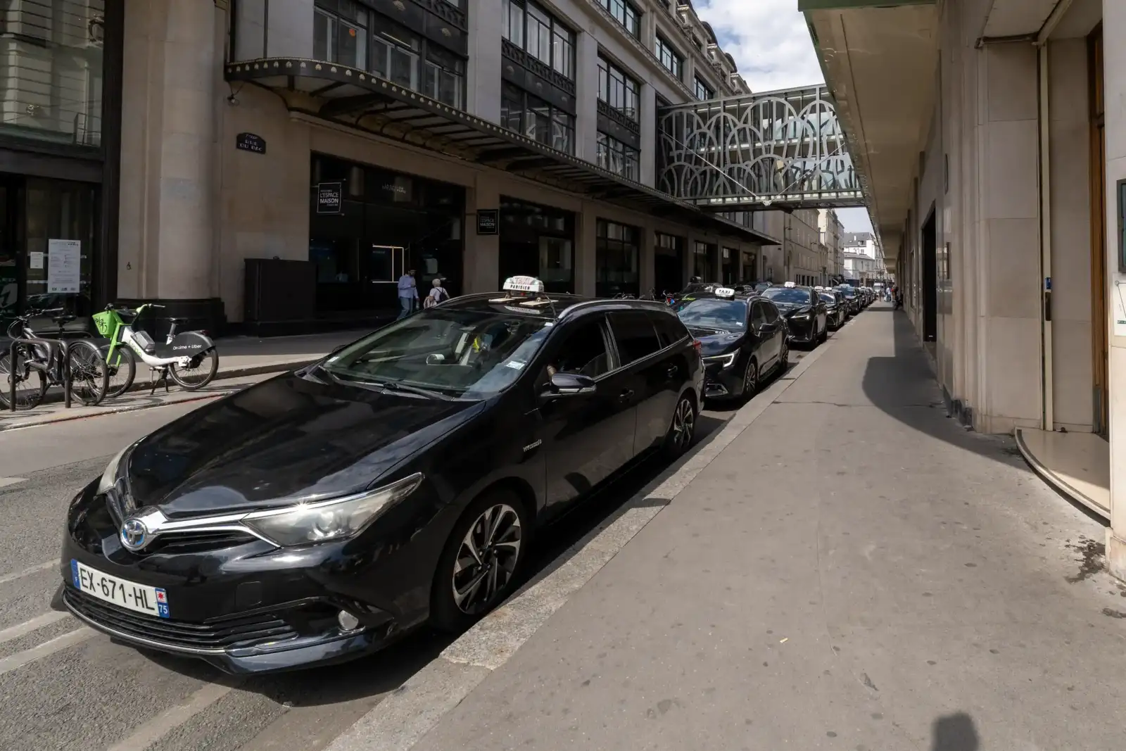 Une file de taxis noirs est garée sous la passerelle vitrée parisienne.