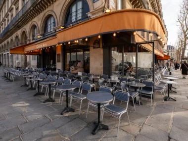 Terrasse d'un café parisien avec des tables et chaises sur un trottoir ensoleillé.