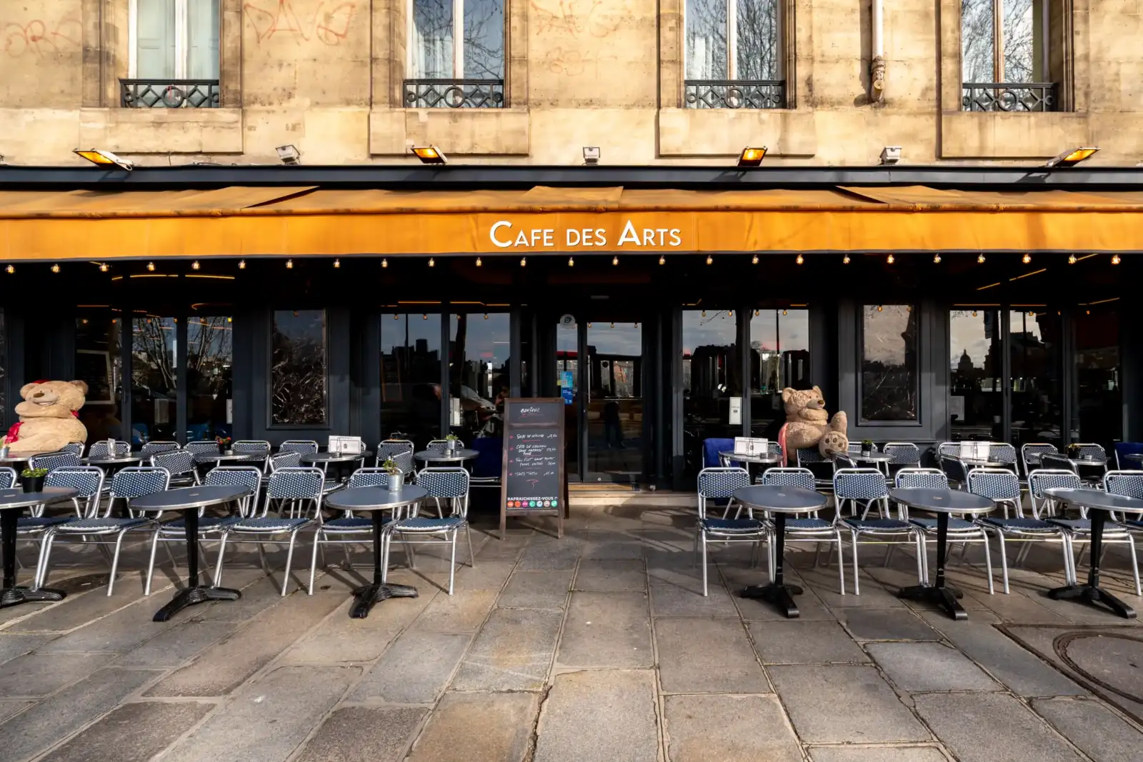 Terrasse d'un café parisien avec des chaises et deux grands ours en peluche.