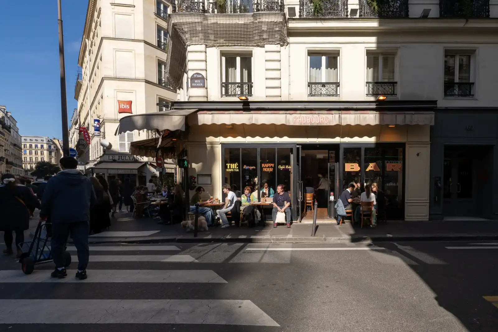 Une terrasse de café parisien animée située à l'angle d'une rue ensoleillée.