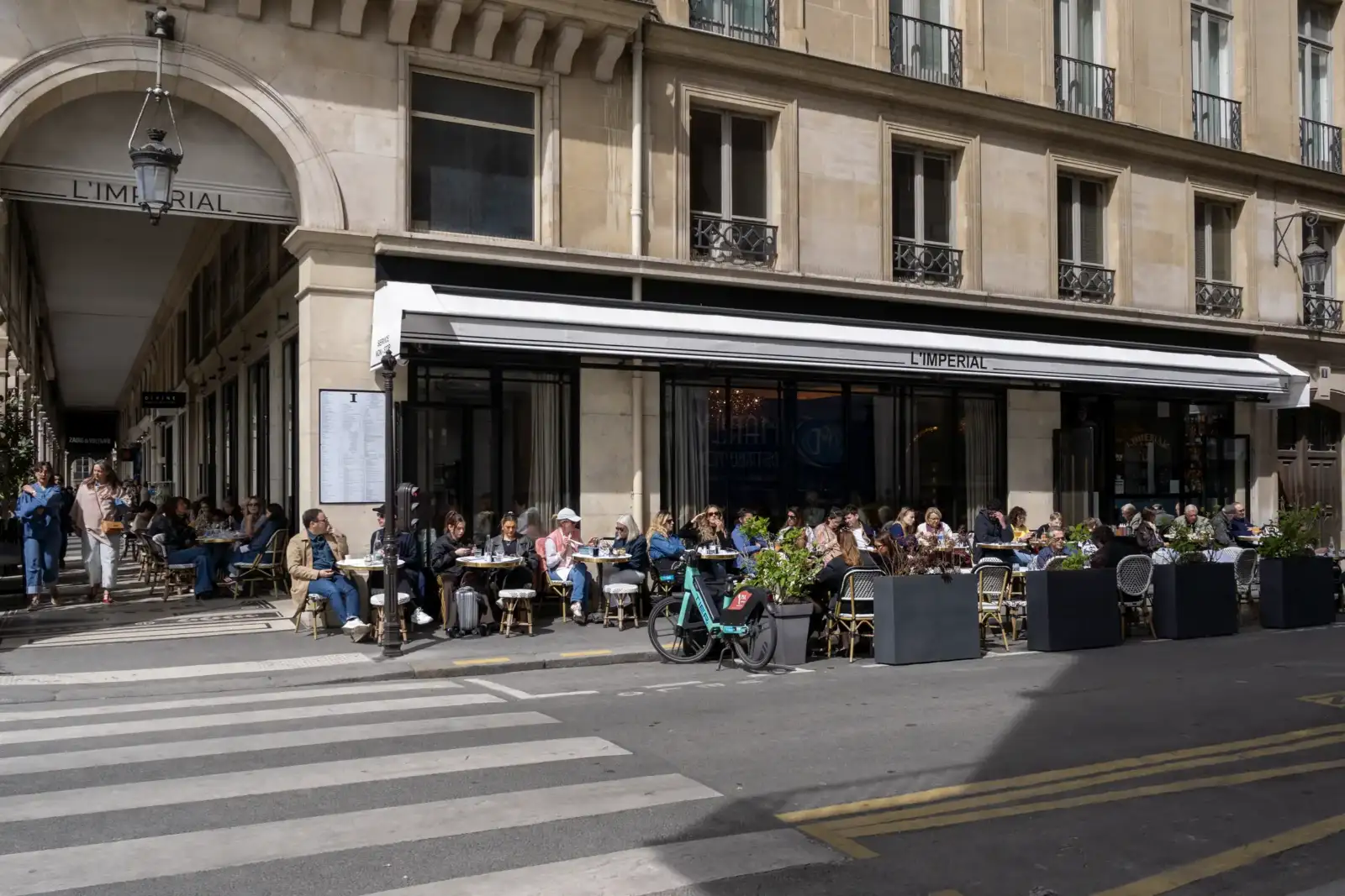 Une terrasse de café parisien animée devant une élégante façade en pierre de taille.