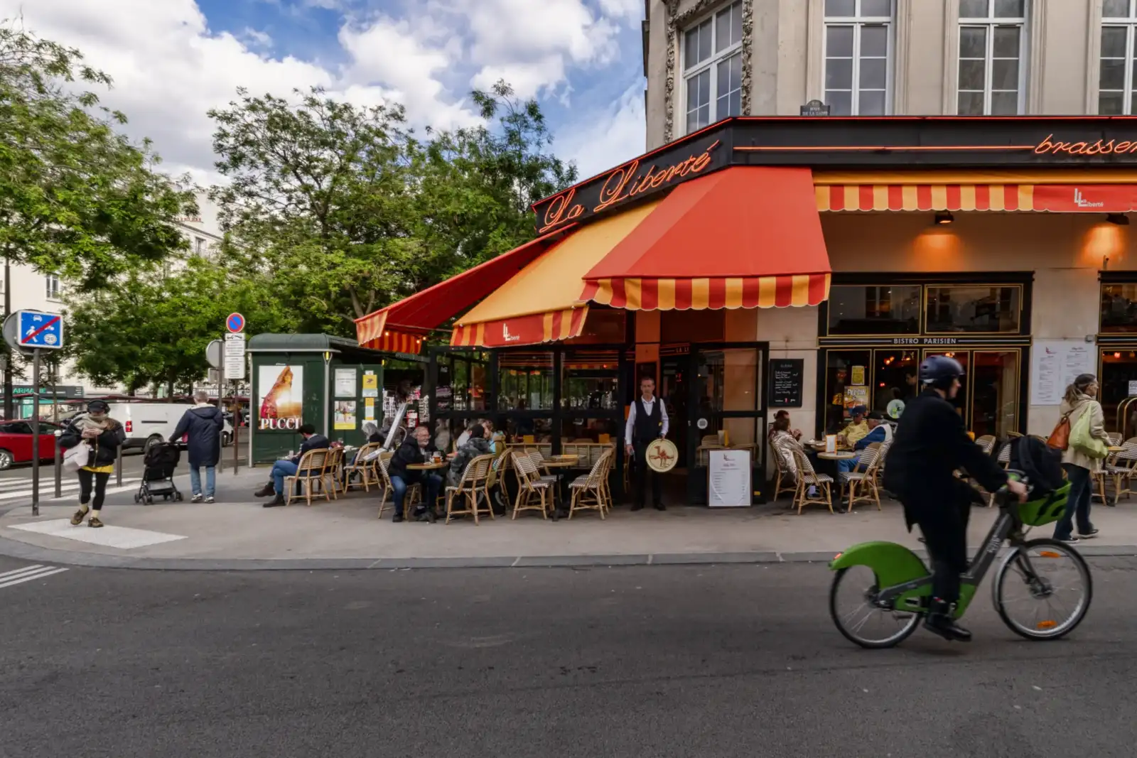 Une terrasse de café parisien animée avec des clients sous des stores colorés.