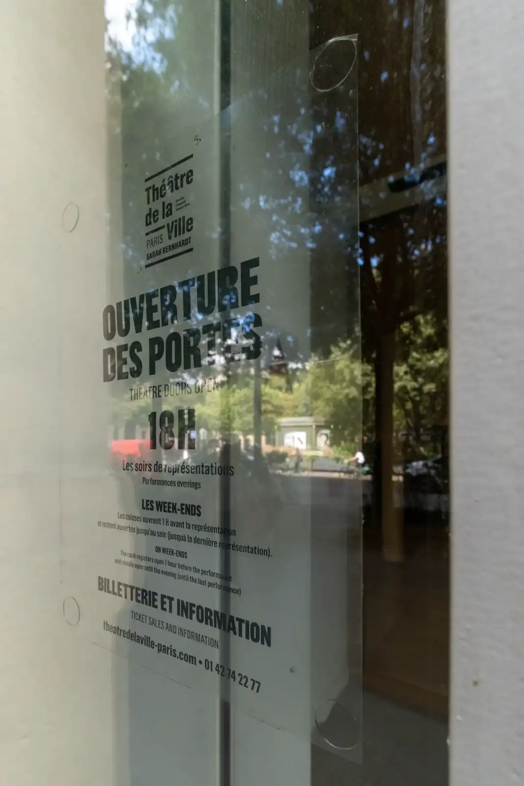 Une affiche transparente sur une porte de verre annonce l'ouverture des portes du Théâtre de la Ville.