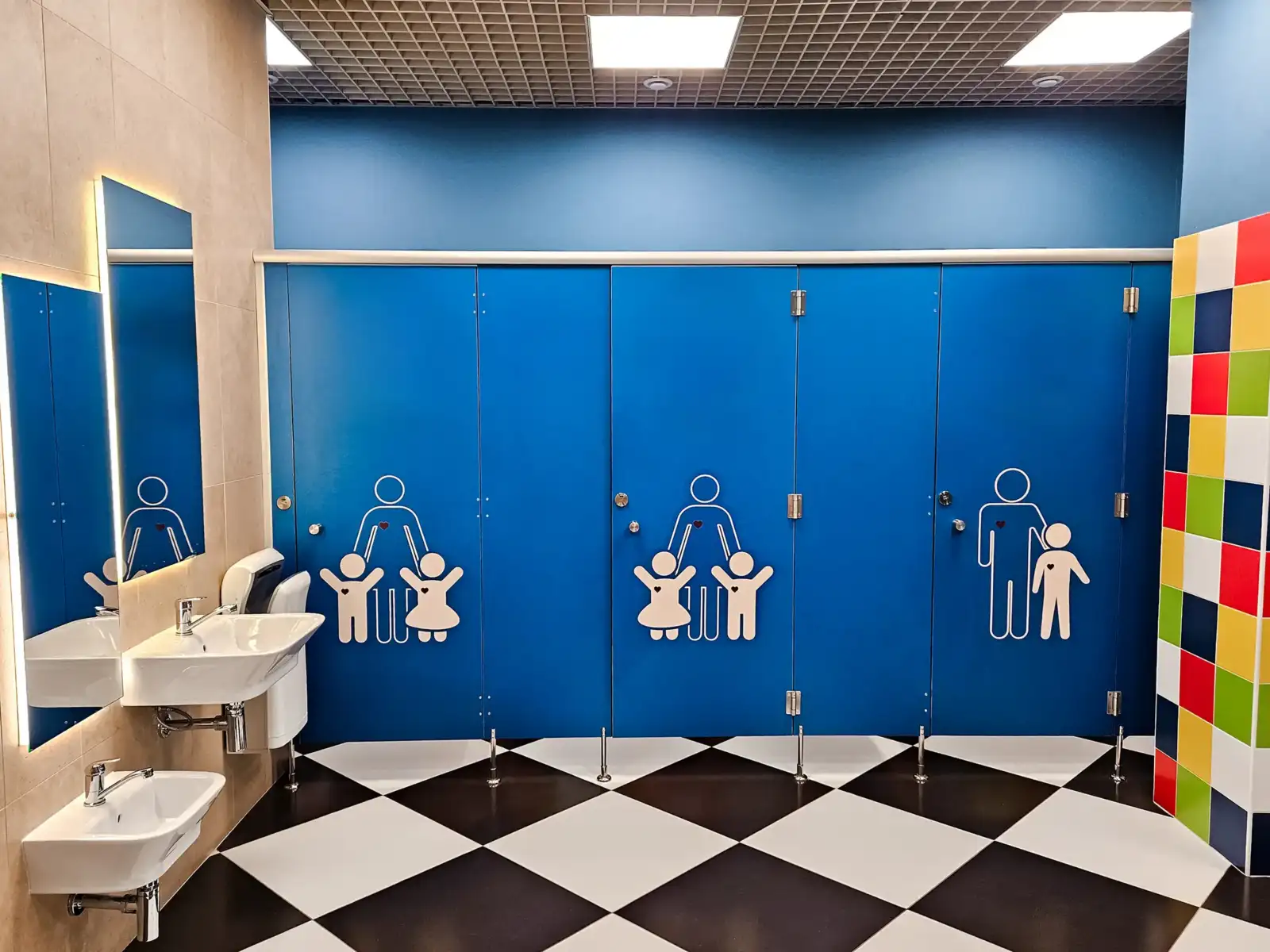 Des toilettes publiques bleues pour enfants avec des pictogrammes familiaux et un carrelage noir et blanc.