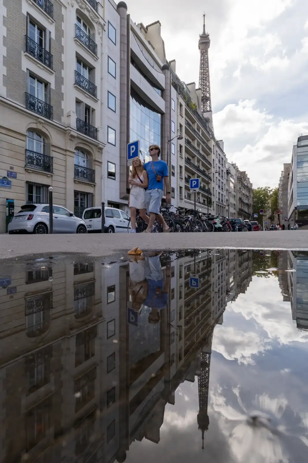 Un couple marche dans une rue parisienne avec la Tour Eiffel visible en arrière-plan.