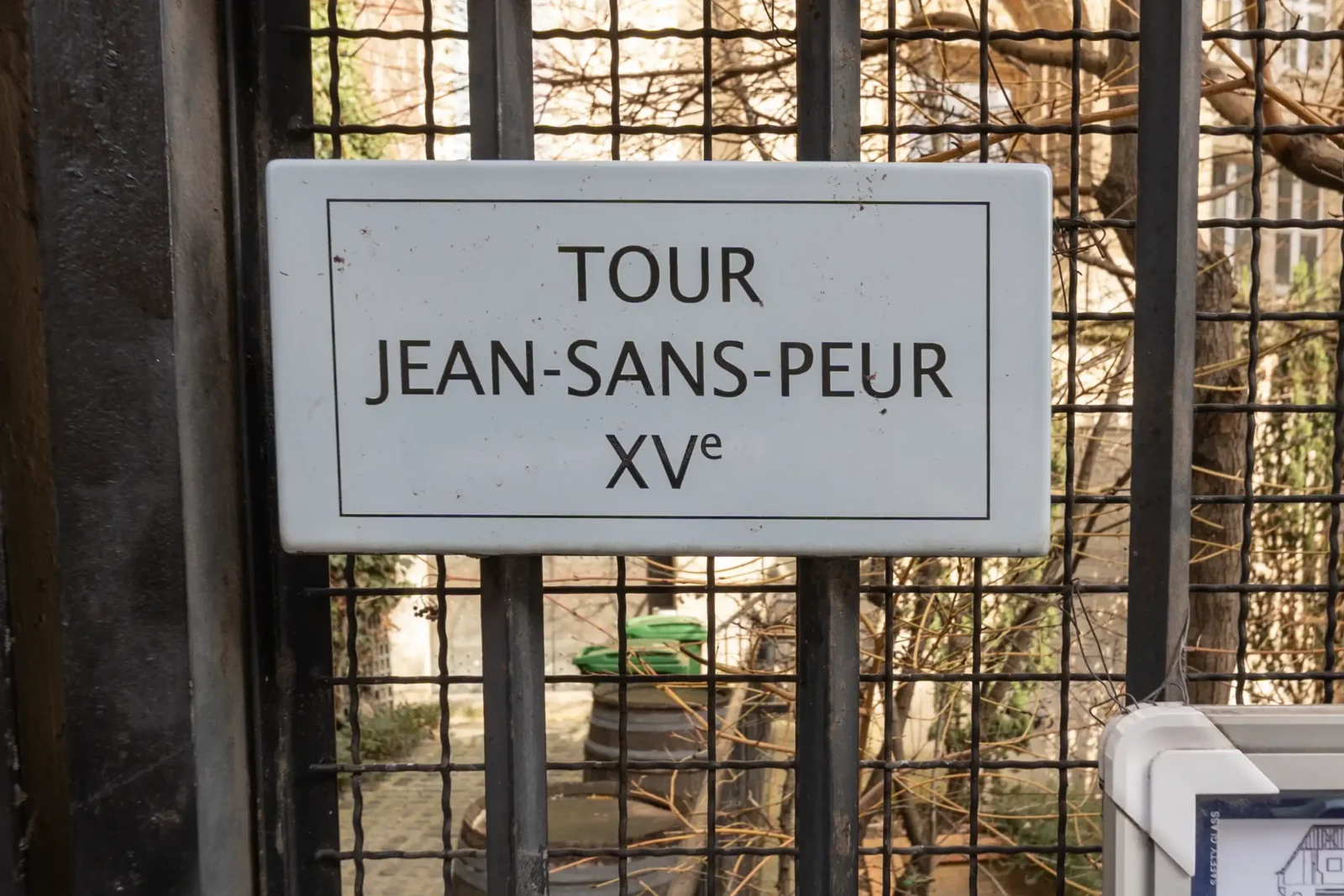 Panneau signalétique blanc indiquant Tour Jean-sans-Peur XVe fixé sur une grille métallique noire.