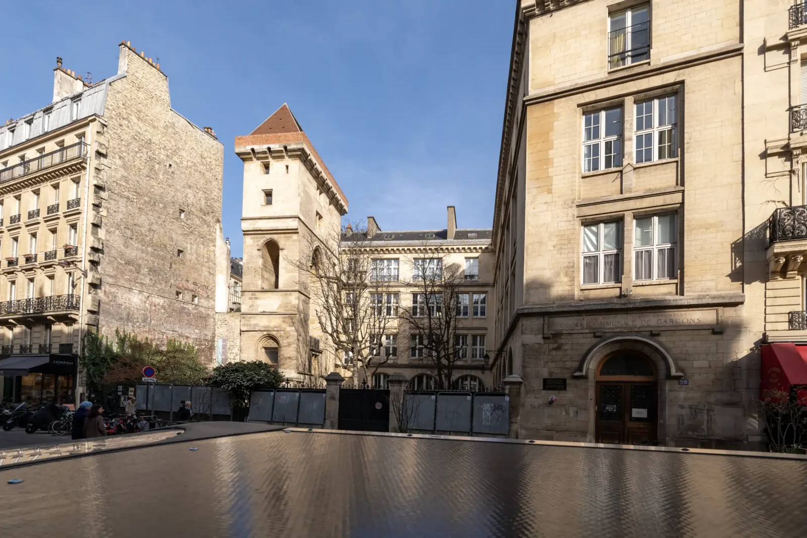 La tour Jean sans Peur s'élève entre des bâtiments parisiens sous un ciel bleu.