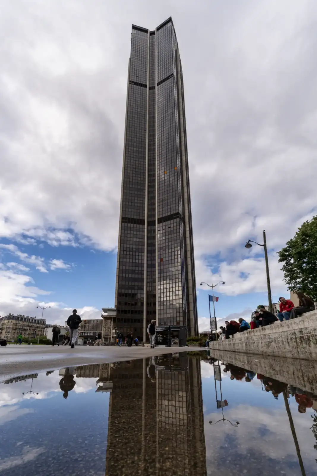 La haute tour Montparnasse sombre et vitrée se reflète dans une flaque d'eau.