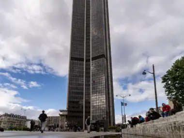 La haute tour Montparnasse sombre et vitrée se reflète dans une flaque d'eau.