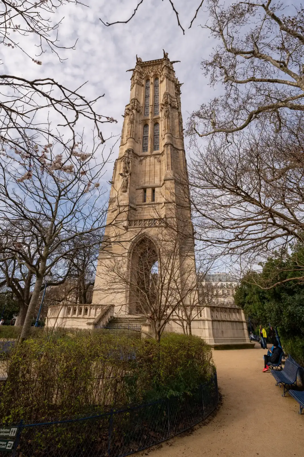 La tour Saint-Jacques se dresse majestueusement au-dessus d'un parc parisien par une journée ensoleillée.