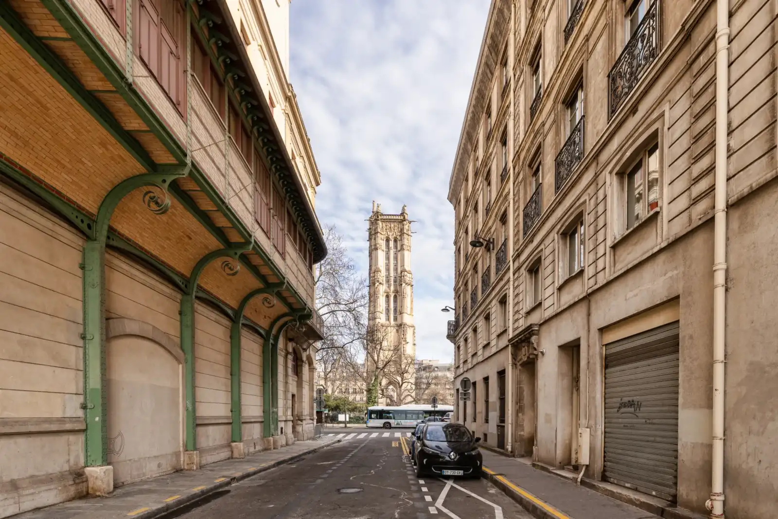La Tour Saint-Jacques se dresse au bout d'une rue parisienne bordée d'immeubles anciens.