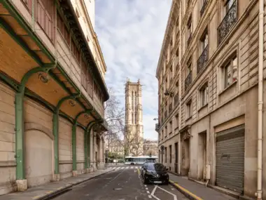 La Tour Saint-Jacques se dresse au bout d'une rue parisienne bordée d'immeubles anciens.