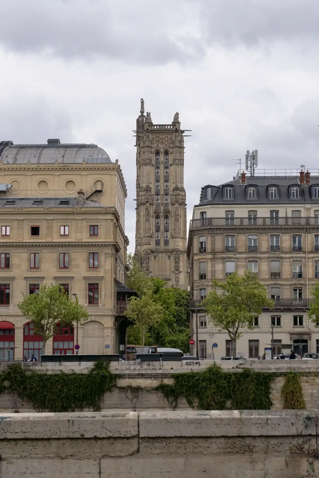 La tour Saint-Jacques s'élève majestueusement entre des immeubles parisiens sous un ciel nuageux.