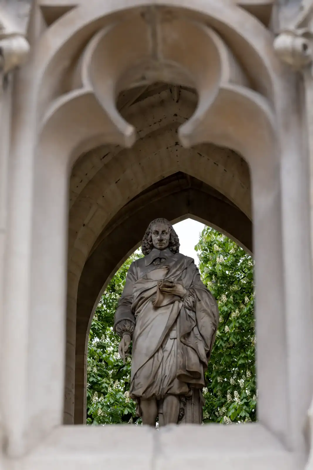 Une statue en pierre encadrée par une arche gothique devant des arbres verdoyants.