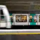 Un train de métro parisien passe rapidement devant un quai de station souterraine éclairée.