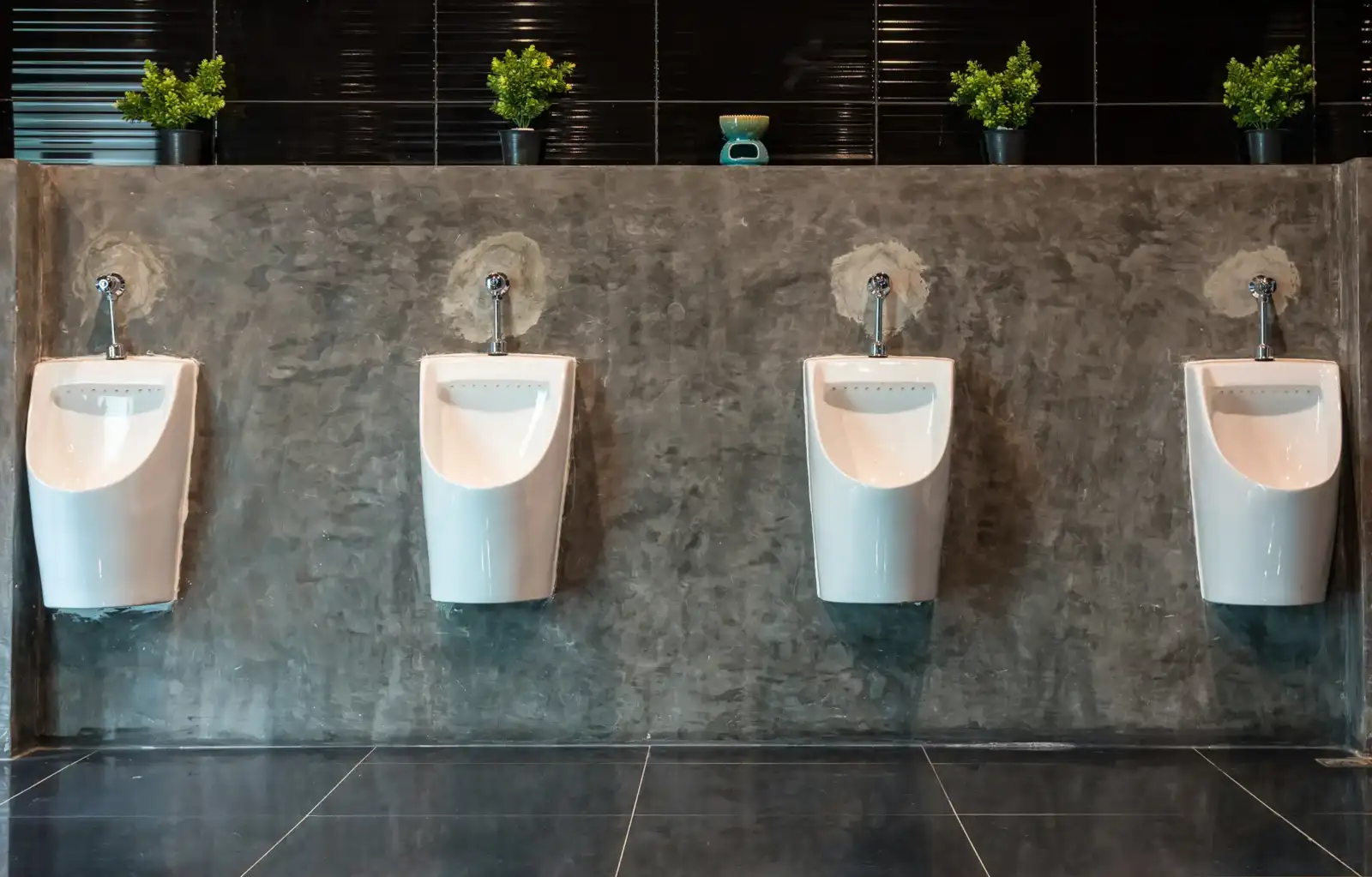 Quatre urinoirs blancs fixés sur un mur en béton ciré dans des toilettes modernes.