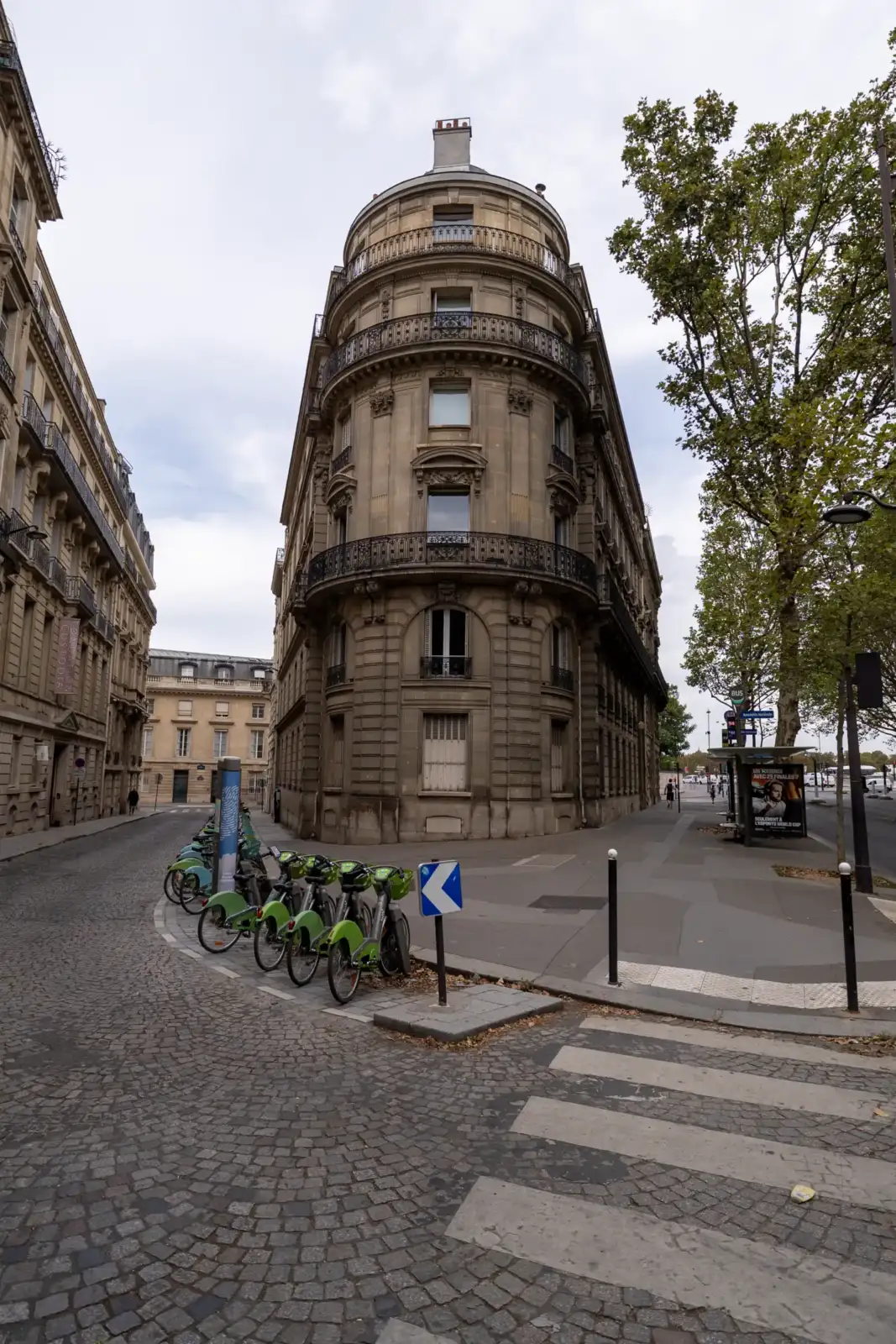 Une rangée de vélos en libre-service stationnés devant une façade parisienne traditionnelle.